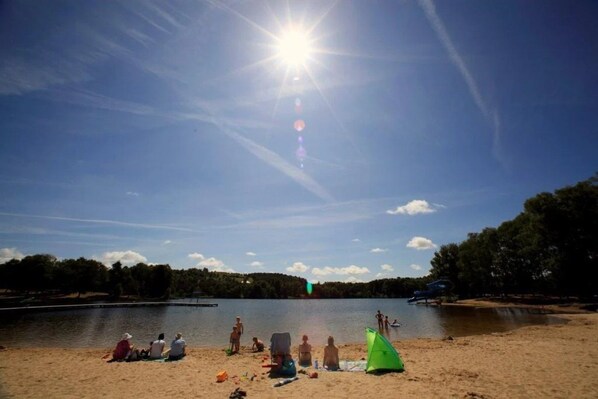 A beach with people relaxing, a lake, and a clear sky.