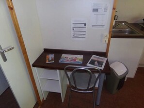 A small kitchenette with a sink, a chair, and a trash bin.