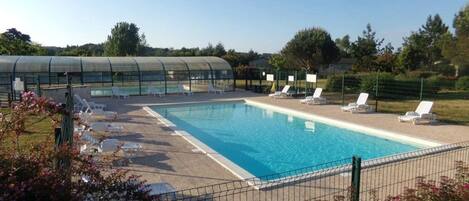 A swimming pool with lounge chairs and a greenhouse structure in the background.