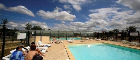 Zona de piscina con sillones de descanso y un área de estar cubierta.