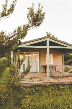 Een gelijkvloers houten huis met een schuin dak, grote ramen en een houten terras.
