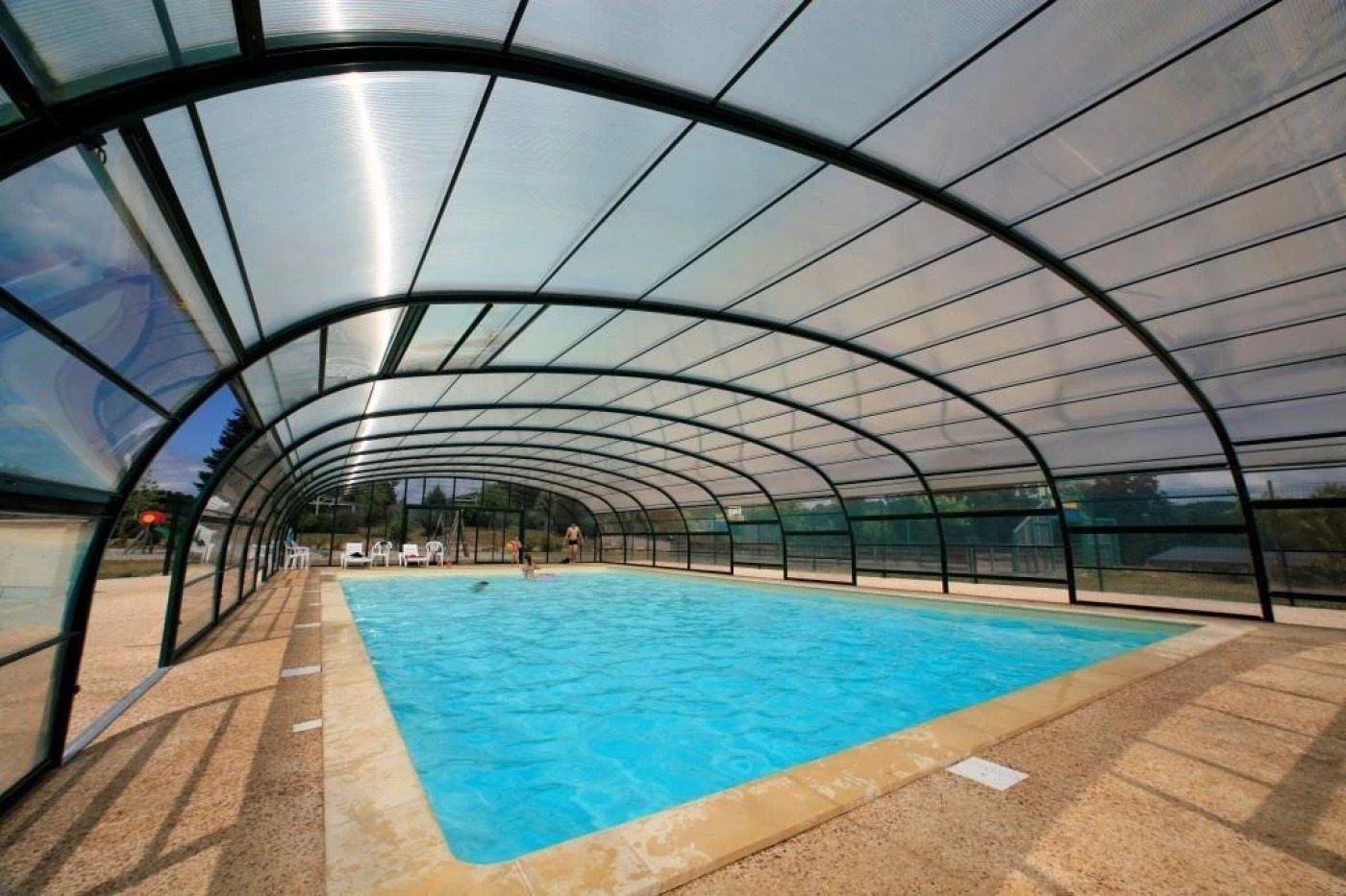 An indoor swimming pool with a curved glass roof, surrounded by a sandy floor.