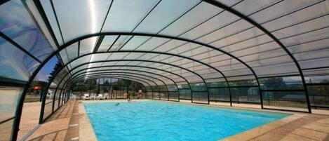 An indoor swimming pool with a curved glass roof, surrounded by a sandy floor.