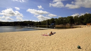 Une plage de sable avec un lac paisible, une jetée et quelques personnes.