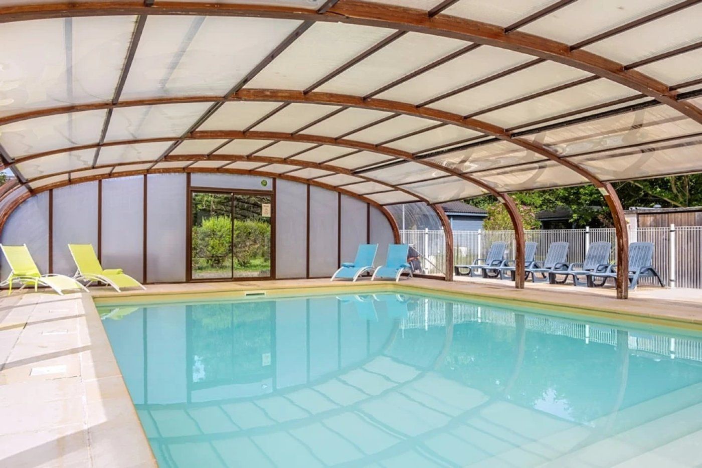 A covered swimming pool with lounge chairs and a view of the outdoors.