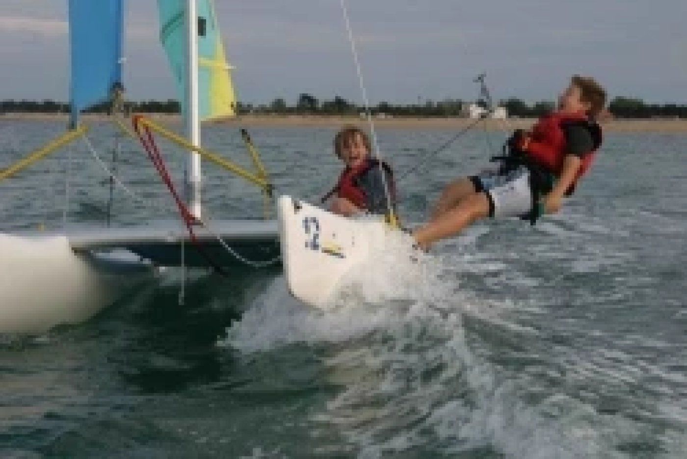 A sailboat with a person lying on the deck, another person standing, and a third person in the water.