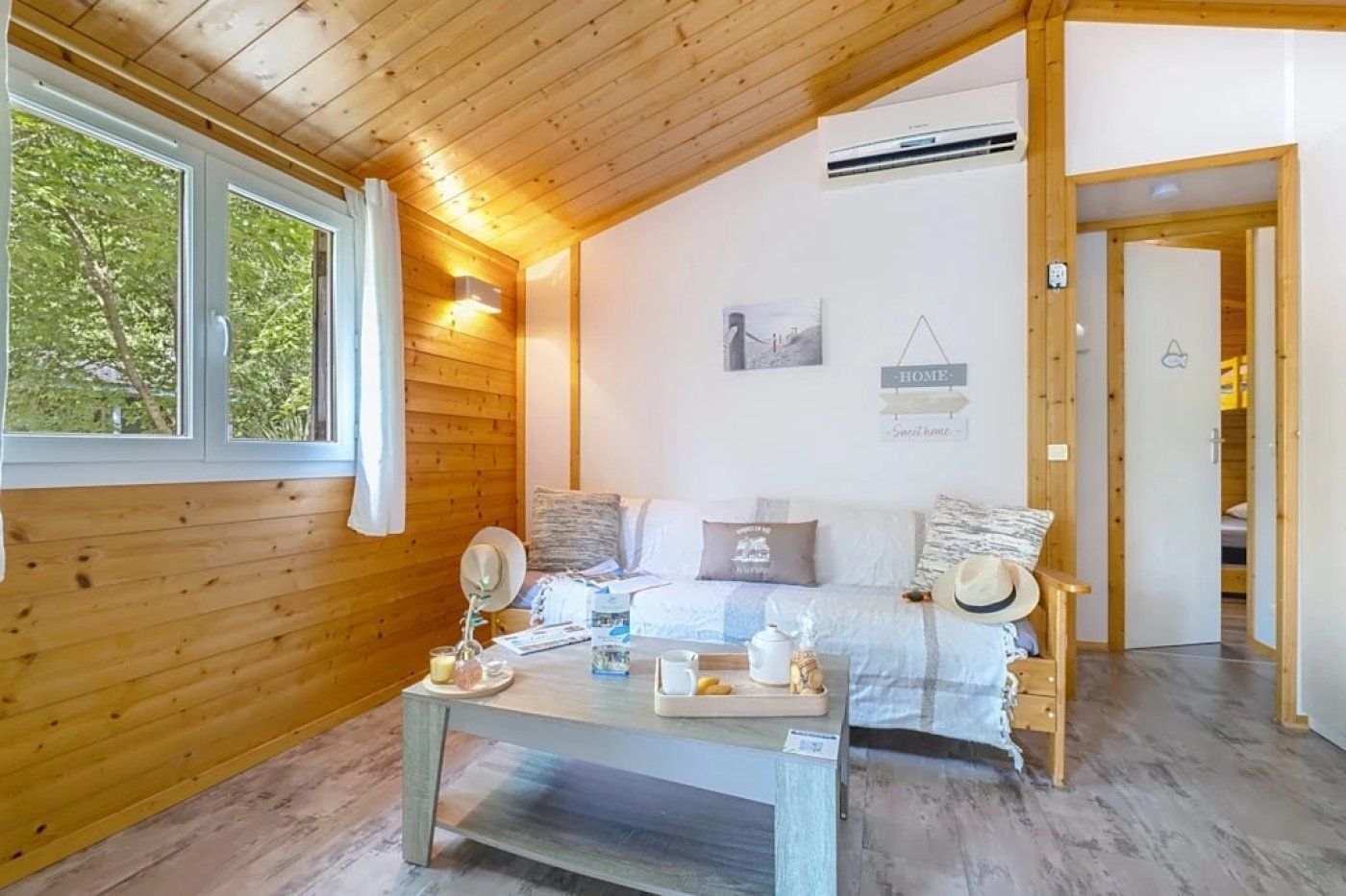 A cozy room with a wooden ceiling, a bed with pillows, a bedside table with a lamp, and a window with curtains.