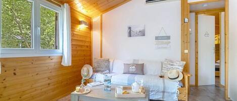 A cozy room with a wooden ceiling, a bed with pillows, a bedside table with a lamp, and a window with curtains.