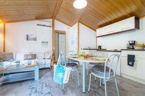 A cozy room with a bed, a dining table with chairs, a kitchen area with cabinets, and a wooden ceiling.