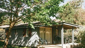 Ein kleines, eingeschossiges Haus mit überdachter Veranda, einer Schiebetür und einer kleinen Sitzgelegenheit im Freien.