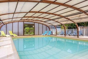Una piscina techada con sillas de descanso y vista al exterior.