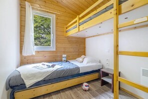 A bunk bed room with a window, a bedside table, and a small shelf.