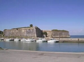 A large fort-like structure by the sea with several boats docked in the water.
