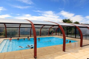 Una piscina interior con cerramiento de vidrio y suelo de baldosas.