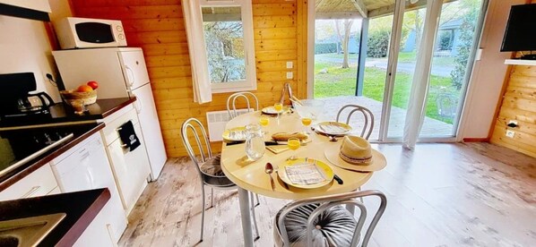 A dining area with a table set for four, a kitchen area with appliances, and a view of the outdoors through a glass door.