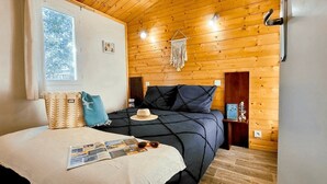 Ein gemütliches Schlafzimmer mit Holzboden, einem Bett mit dunkelblauer Bettdecke, einem weißen Kissen und einem Hut auf dem Bett.