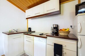 Una cocina funcional con armarios blancos, microondas, cafetera y una cesta de frutas.