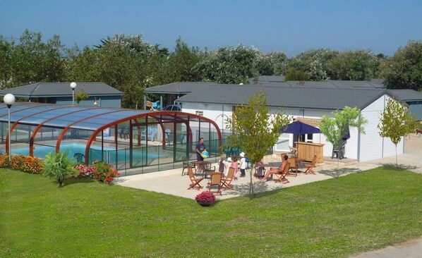 Zona de piscina con cerramiento de vidrio, mobiliario exterior y un edificio de techo inclinado.