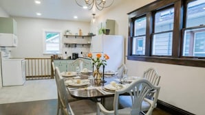 Un coin repas avec une table en bois dressée pour quatre personnes, des chaises blanches et un vase rempli de fleurs oranges.