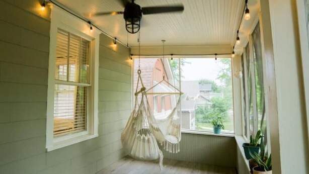 Une pièce dotée d’un ventilateur de plafond, d’un fauteuil suspendu et offrant une vue sur la verdure environnante.