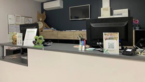 A reception desk with a computer, a large teddy bear decoration, a wall-mounted air conditioner, and a welcome sign.