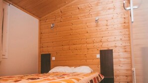 A single bed with a patterned blanket in a room with wooden walls and a sloped ceiling.