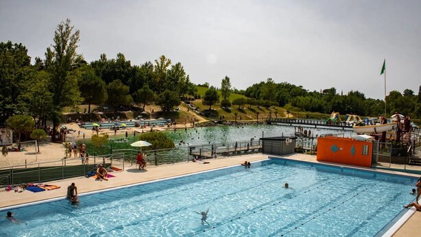 A swimming pool with clear water, surrounded by a sandy beach area and trees.