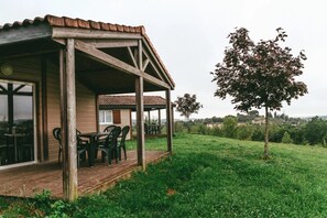 Un bâtiment en bois doté d’un patio couvert, d’un espace extérieur aménagé avec des sièges et d’une zone herbeuse avec des arbres.