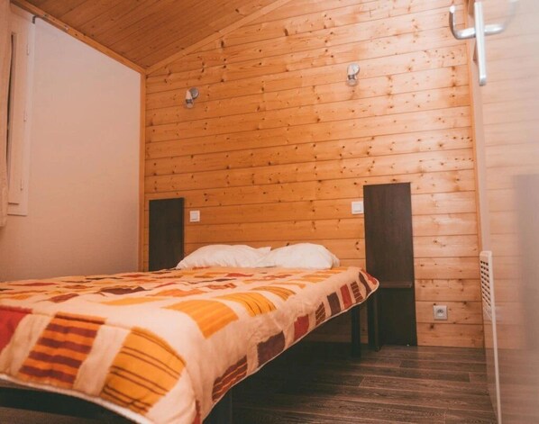 A single bed with a patterned blanket in a room with wooden walls and a sloped ceiling. - ZEcamping 3 étoiles dog friendly avec piscine couverte et chauffée (Monclar-de-Quercy)