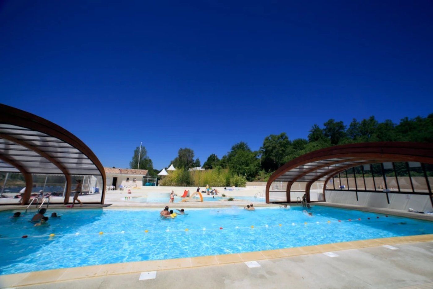 A swimming pool with two covered areas on either side, surrounded by trees and a clear sky.