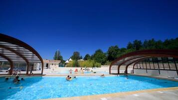 A swimming pool with two covered areas on either side, surrounded by trees and a clear sky.