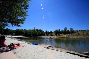 A lakeside setting with a sandy beach, a dock, and a clear sky.