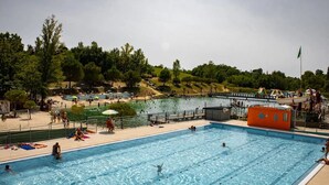 A swimming pool with clear water, surrounded by a sandy beach area and trees.