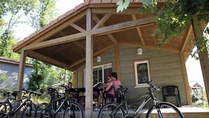 Ett takförsett utomhusområde med en träkonstruktion, cyklar och en person som sitter på en bänk.