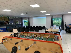 A room with a foosball table, a projection screen, and a view of greenery outside.