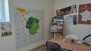 Une pièce avec une grande carte accrochée au mur, un tableau d’affichage où sont fixés divers objets, et une table avec une chaise.