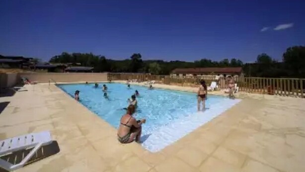 Un área de piscina con varias personas nadando y otras en el borde de la piscina.