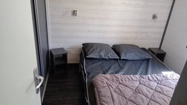 A bedroom with a bed, a nightstand, a drawer unit, and a door.