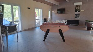 Una habitación amplia con mesa de fútbol, televisor en la pared y ventana que proporciona luz natural.