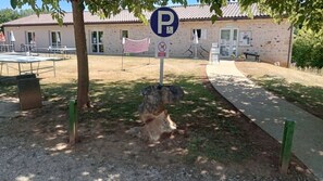Señal de estacionamiento con el símbolo de accesibilidad para sillas de ruedas, un letrero de prohibido fumar y un edificio con techo de tejas al fondo.
