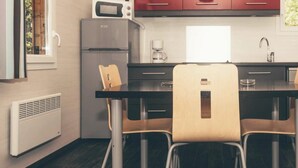 A compact kitchen with a microwave, refrigerator, and red cabinets. There is a dining table with two chairs and a window providing natural light.