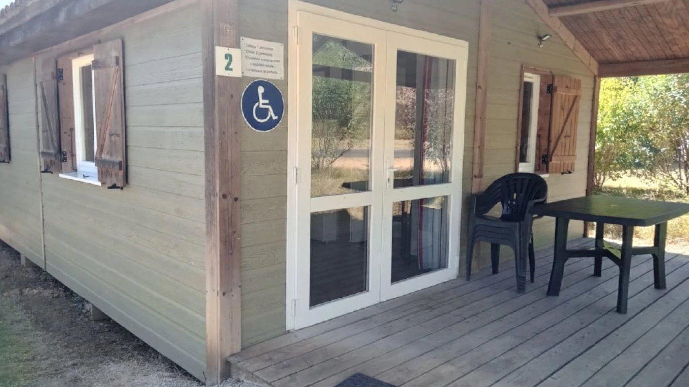 A wooden building with a wheelchair-accessible entrance, a covered outdoor seating area with a table and chairs, and a number sign indicating the room.