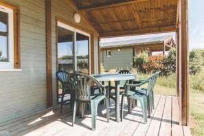 A covered outdoor area with a table and chairs, a wooden deck, and a view of a house with solar panels.