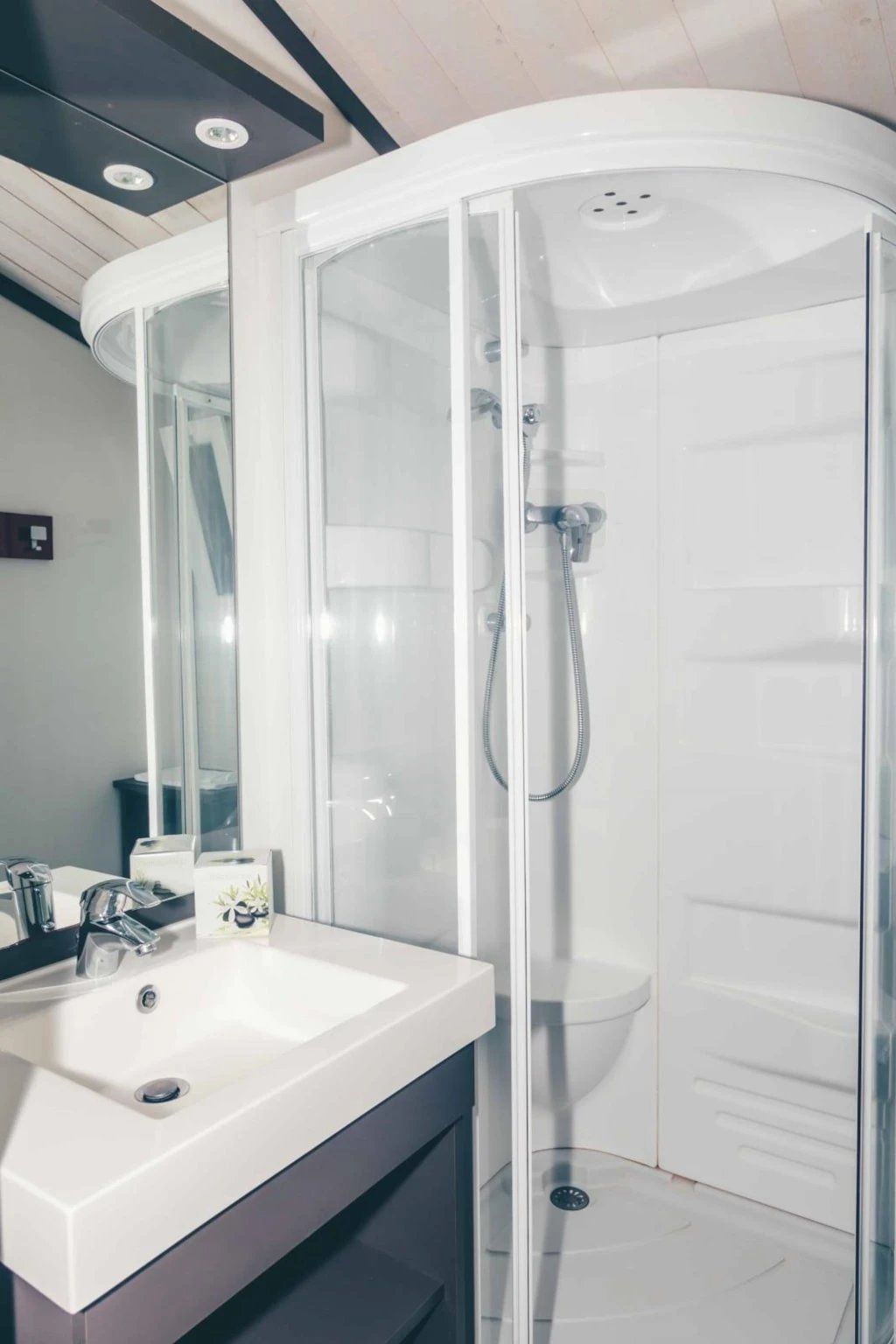 Een moderne badkamer met een douchecabine van glas, een witte wastafel en een spiegel.