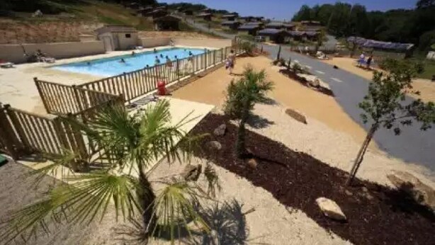 A pool area with a sandy beach, palm trees, and a fenced swimming pool.