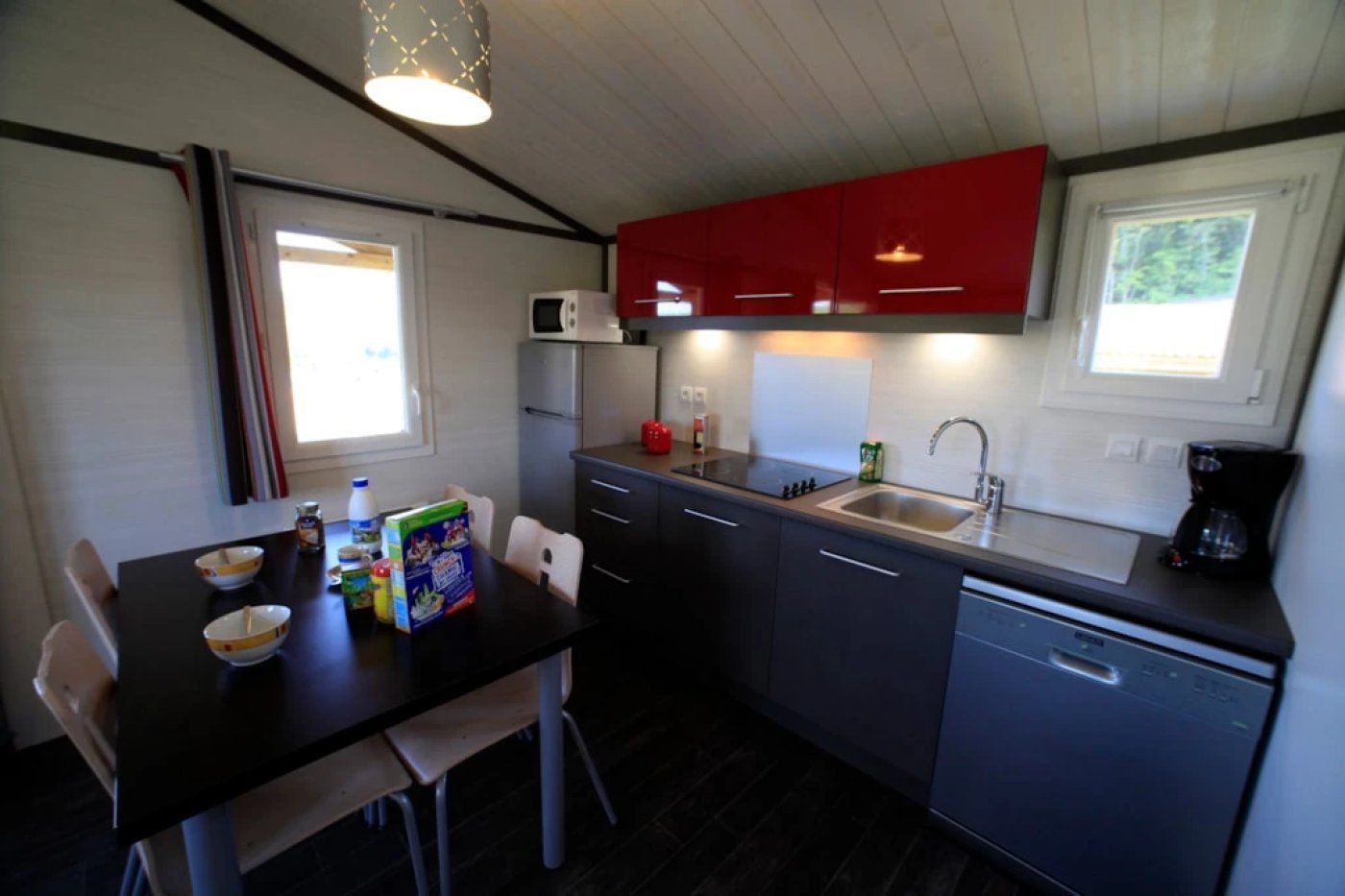 Een compacte keuken met een eettafel, stoelen, een magnetron, een spoelbak en kastjes.