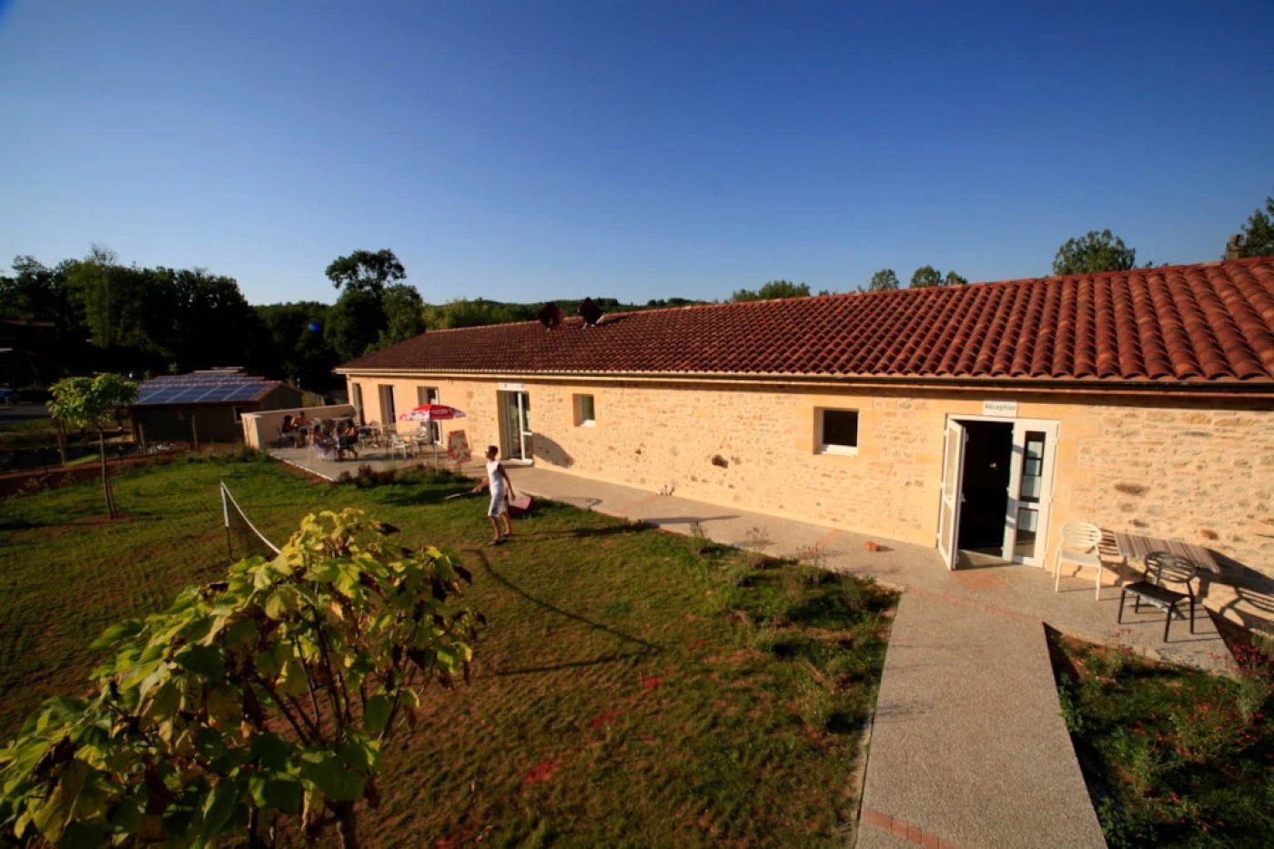A stone building with a tiled roof, a paved entrance, and outdoor seating.