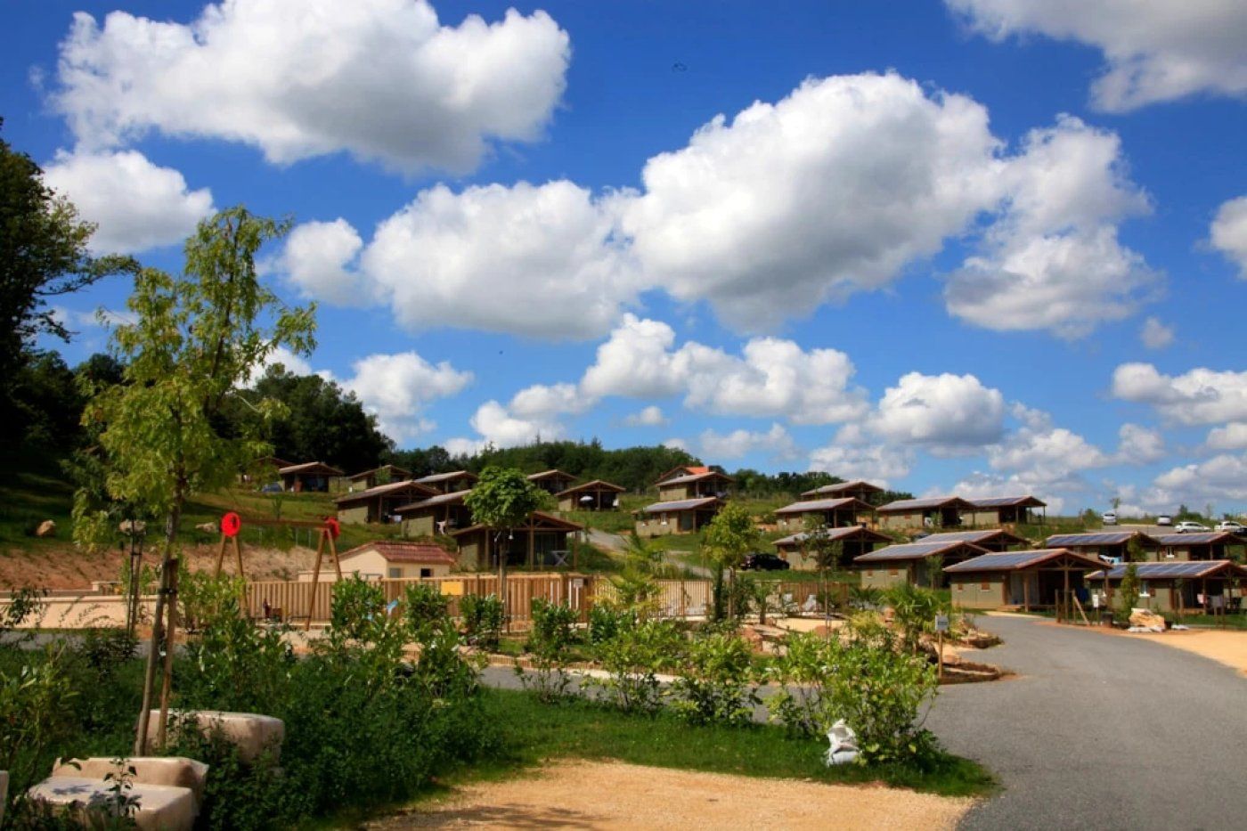 A series of wooden cabins with solar panels, surrounded by greenery and a clear sky.