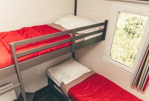A bunk bed with red bedding, a window with a view of greenery, and a bookshelf with books.