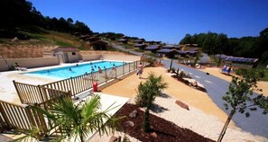 Zona de piscina con un muelle de madera, un sendero de arena y paneles solares en los techos de edificios cercanos.
